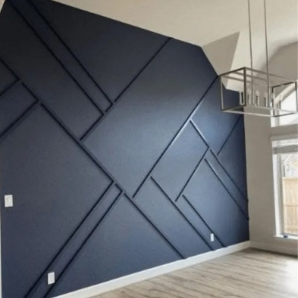 Mur d'accent intérieur peint en bleu marine profond avec un motif géométrique créé par des lattes de bois en relief. Le sol est en parquet clair et un luminaire moderne en métal est suspendu au plafond. Une grande fenêtre apporte de la lumière naturelle sur la droite.